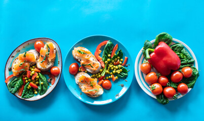 Photocomposition: breakfast: sandwich with salmon, herbs and vegetables, on a blue background, top view