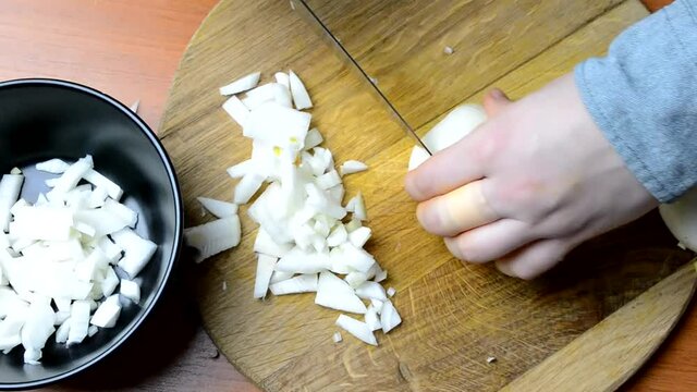 An overhead view of male hands chopping onions on a wooden board in HD