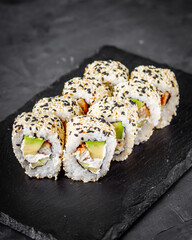 appetizing sushi roll california with eel avocado cucumber and sesame seeds on a black stone plate