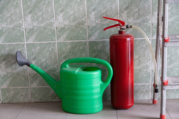 Watering can and fire extinguisher stand in front of wall © glebchik