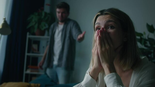 Young woman holding her head and crying close-up. Emotional man shouting at wife in living room, feeling anger and stress, bad mood. Scandals, hysteria and quarrels in family, relationship crisis.