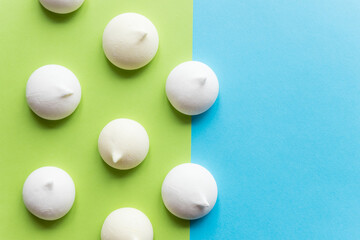 Pattern with delicate white meringue cookies. Meringues are lying in rows on blue green paper background. Unhealthy food concept. Minimal food concept. dessert design mockup, confectionery.