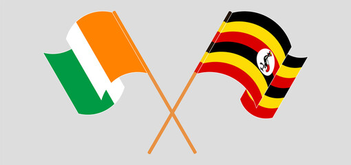 Crossed and waving flags of Republic of Ivory Coast and Uganda
