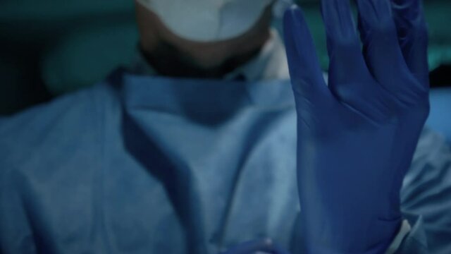 Cinematic Slow-motion of Male Surgeon Doctor Putting On Protective Medical Protective Blue Surgical Gloves in Hospital. Doctor Wearing Face Mask. Concept of Coronavirus Pandemic or Covid-19 Outbreak