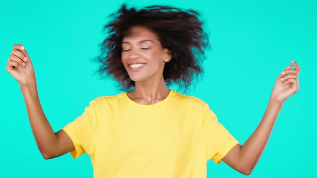 Happy curly haired african woman dancing, having fun, rejoices on teal studio background. Champion girl. Concept of celebrating, party, winning