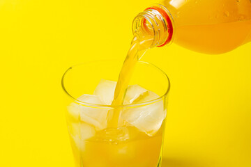 Carbonated orange juice is poured into a glass with ice. Refreshing drink on a yellow background.