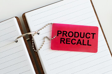 On the card text Product Recall which lies on an open blank notebook