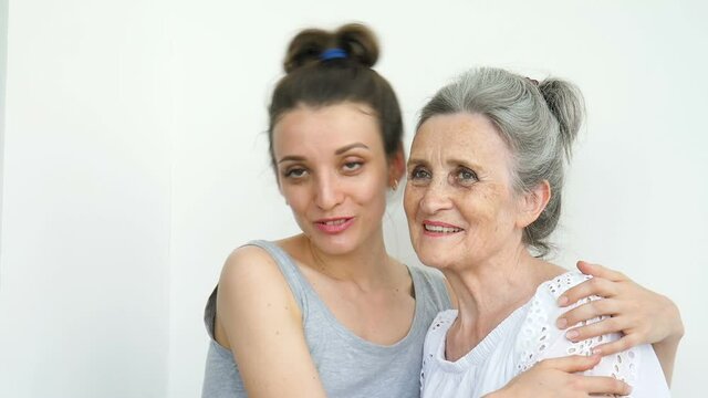 Happy senior mother is hugging her adult daughter, the women are laughing together, sincere family of different age generations having fun on white background