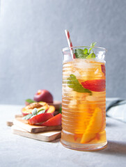 cool peach tea with mint and ice in a glass on a blue background. Front view and copy space