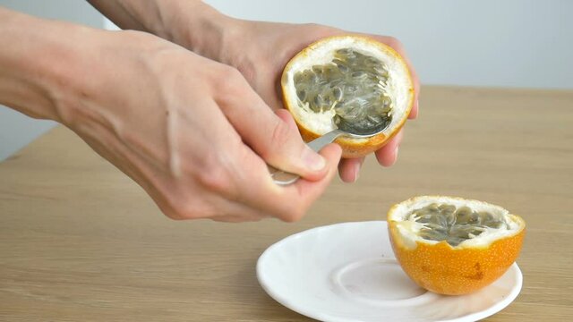 Female eats fresh organic ripe granadilla or yellow passion fruit with a spoon. Exotic fruits, healthy eating concept