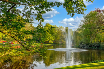 Naklejka premium Fountain on the lake in the flower garden with blooming tulips. Lisse, Netherlands.