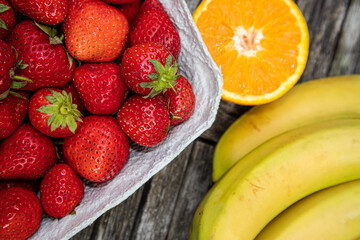 Fototapeta na wymiar Erdbeeren, Orangen und Bananen auf einem Holztisch