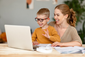 Cheerful mother and son greeting teacher during online lesson at home