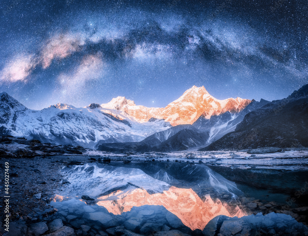 Wall mural milky way over snowy mountains and lake at night. landscape with snow covered high rocks, starry sky