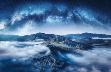 Milky Way arch and mountains in low clouds at starry night in summer. Landscape with sky with...