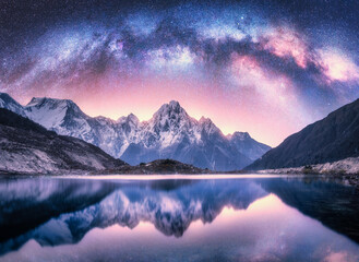 Milky Way over snowy mountains and lake at night. Landscape with snow covered high rocks, purple...