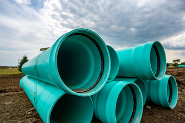 Stacked water main pipe with bell fitting next to an exposed trench for installation