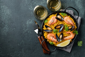 Traditional spanish seafood paella in pan with chickpeas, shrimps, mussels, squid on black concrete background. Top view with copy space