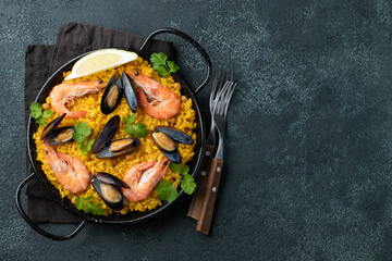 Traditional spanish seafood paella in pan with chickpeas, shrimps, mussels, squid on black concrete background. Top view with copy space