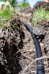 Focus on a black 1 inch sprinkler plastic water line laid in a shallow trench