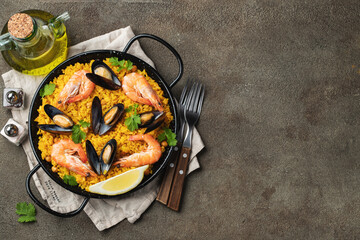 Traditional spanish seafood paella in pan with chickpeas, shrimps, mussels, squid on brown concrete background. Top view with copy space