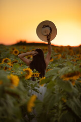 A happy, beautiful young girl with long hair in a straw hat is standing in a large field of...