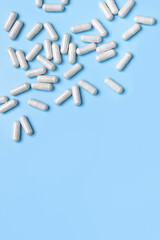 Pills, tablets, vitamins, food supplement in white capsules on blue background. Health concept, vitamin deficiency, avitaminosis, medical pharmaceutical background. Flat lay top view copy space