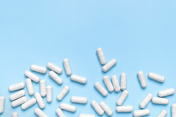 Pills, tablets, vitamins, food supplement in white capsules on blue background. Health concept,...