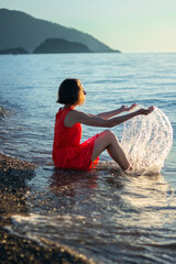 Young woman in red dress posing on the beach at sunrise