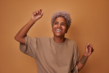 Happy dark skinned woman enjoys music at party dances carefree has fun and moves with rhythm of...