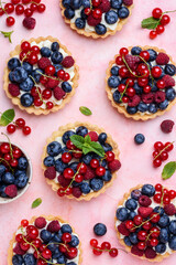Tartlets with curd cream and fresh berries of raspberries, blueberries, red currants. Summer fruit baking. Pink background. Top view