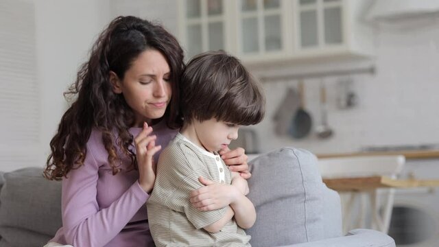 Angry offended aggrieved child son sit with arms crossed avoid mother trying to talk to upset stubborn kid about misunderstanding problem after family quarrel or fight. Worried mom want to say sorry
