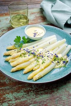Modern style traditional steamed white asparagus garnished with sauce hollandaise and herbs served as close-up on a design plate
