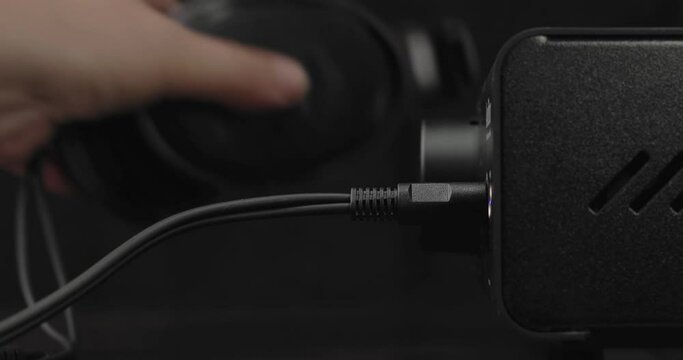 Headphone amplifier and headphones are on the table. The male hand takes the plug and plugs it into the amplifier. Then the person takes the headphones and starts adjusting the volume of the music.