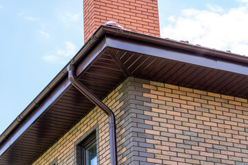 close-up view of house with brown roof and filing of roof overhangs with soffits and brick stone...