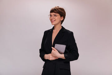Business woman in black suit holds computer tablet. Short-haired employee in dark jacket smiles...