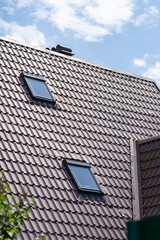 Sloping roof with soft coating of residential building with windows and ventilation with green trees in foreground