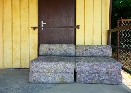 An old couch stands in front of the locked door of an abandoned natural hostel - Powered by Adobe