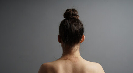 Naked woman with a messy bun hairstyle facing a gray wall