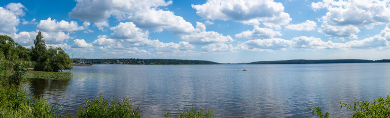 Scenery view of the Baltic Sea Bay on sunny summer day. Rocky shores of Scandinavia covered with evergreen forests. Houses villas on the coast of Sweden. Blue sky white clouds. Reeds on the foreground