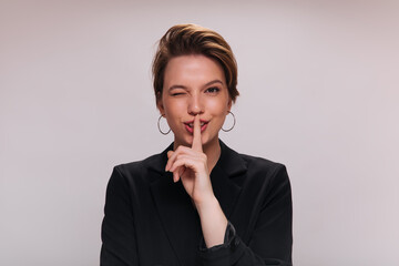 Woman winking and asking for keeping secret. Short-haired lady in stylish jacket posing and looking...