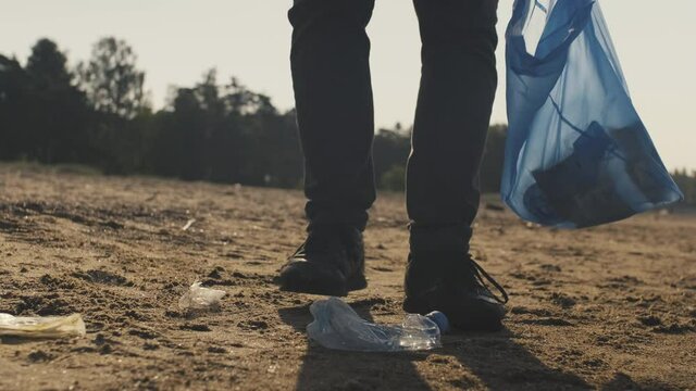 A volunteer guy picking up plastic garbage off sandy beach, forests and camping points to upkeep environment and turn it into pristine condition that earth inhabitants managed to destroy.  
