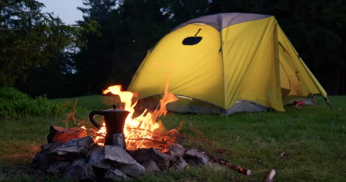 Coffee pot near the fire and tent in the forest glade