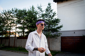 Positive male with bandana dressed in street style clothes with chains around neck and purple bandana for a walk. Youth and lifestyle concept. Rap artist new school. Smoking cigarette.