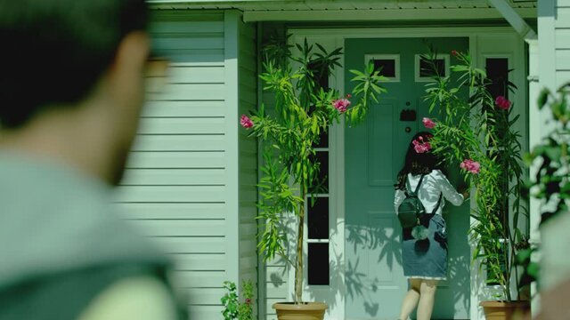 Back rear view stranger man following young girl while she walking on way to home . Girl opens door and enters inside house  boy secretly follows , spying behind . Boyfriend tracking of his girlfriend