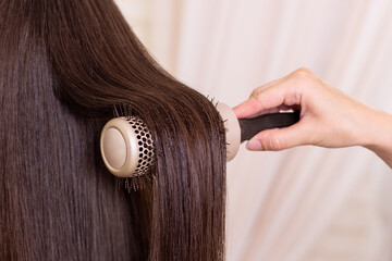 Hairdresser's hand brushing long brunette hair in beauty salon