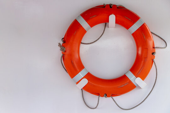 Safety concept, Selective focus of lifebuoy hanging on white wall, Old used red ring buoy with the rope on the boat, Water wheely is a life saving buoy designed to be thrown to a person in the water.