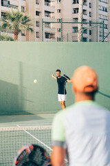 Fototapeta na wymiar Man training paddle tennis on an outdoor green paddle tennis court behind the net with his coach