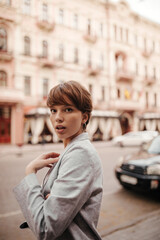 Fototapeta premium Brown eyed woman in grey jacket looking into camera outside. Happy girl in stylish oversize suit walking around city in good mood