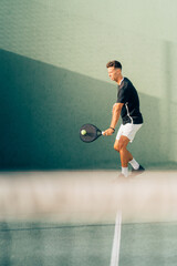 Man playing paddle tennis on an outdoor green paddle tennis court at the sunset
